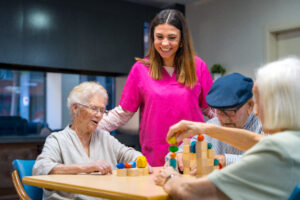 seniors building towers with caregiver at table We Care Online Is Now an NCCAP Approved Educator