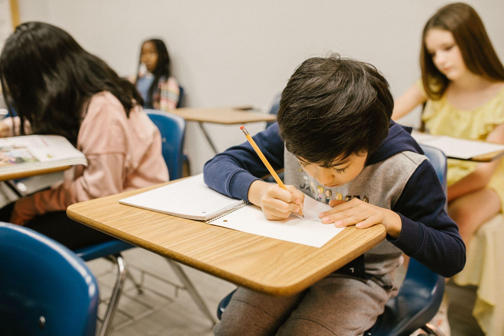 Student writing in a notebook at a classroom desk